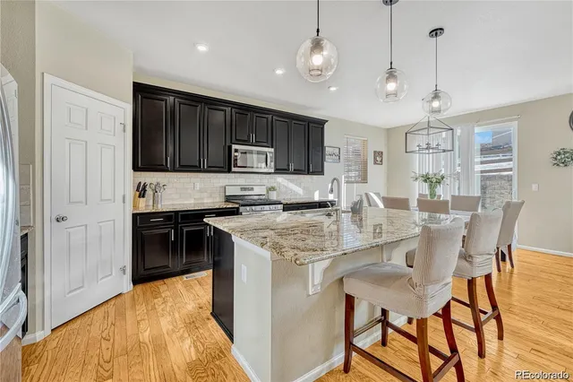 a open kitchen with stainless steel appliances granite countertop a stove top oven a refrigerator a sink and a dining table with wooden floor