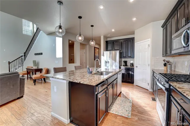 a kitchen with granite countertop a stove a sink a refrigerator and a living room view