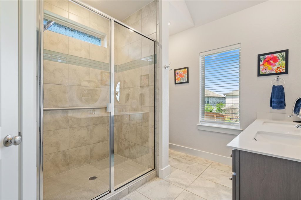 7912 Prairie Rye Drive Lago Vista, TX 78645 - Photo 18 of 37 Primary ensuite bath featuring a spacious double vanity, modern lighting, and a large walk-in tiled shower with glass enclosure. Enjoy ample storage and natural light in this serene, spa-like retreat.