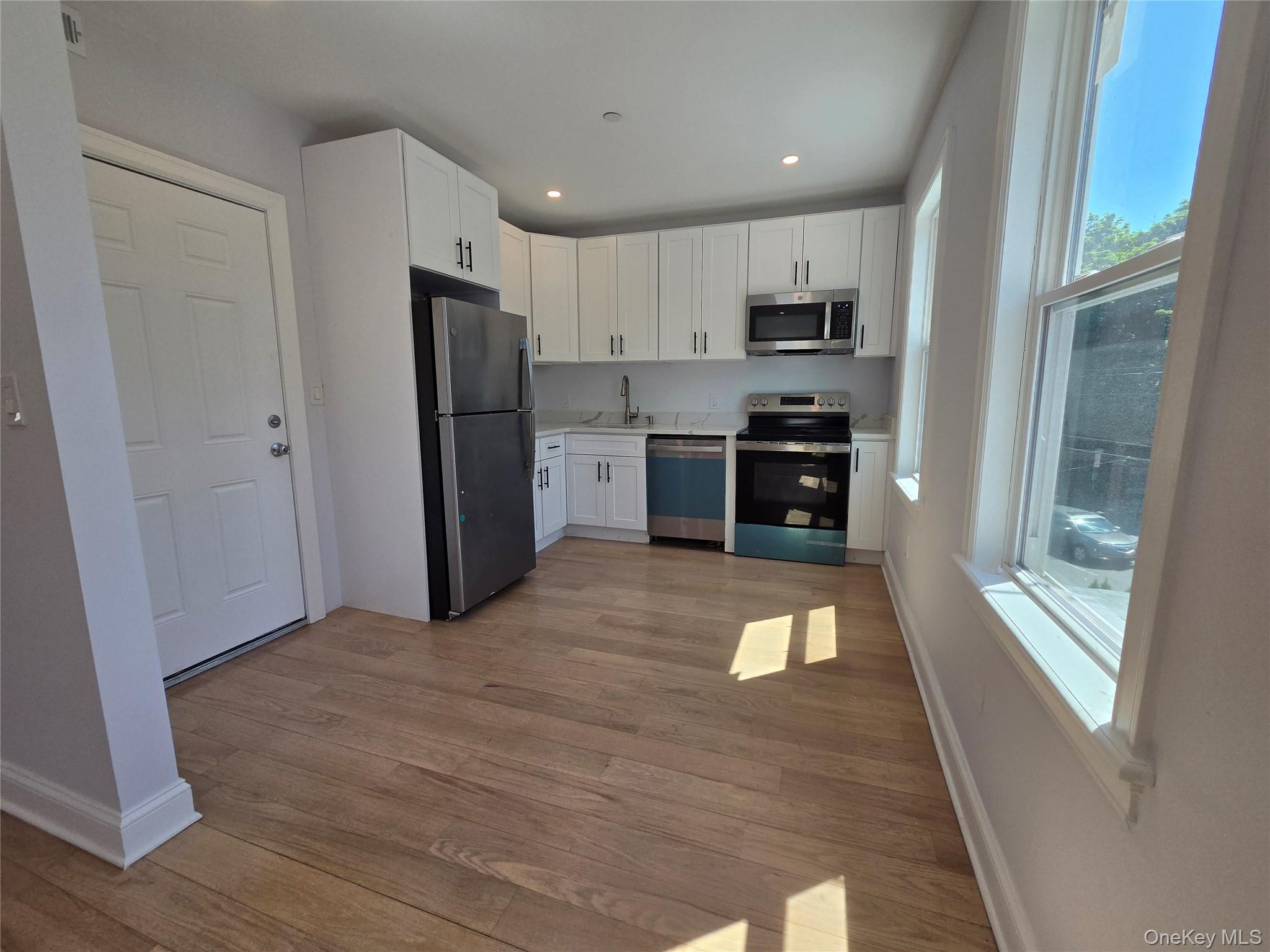965 Main Street, Unit 2 New Rochelle, NY 10801 - Photo 2 of 12 Kitchen featuring wood-finish flooring, white cabinetry, stainless steel appliances, and multiple windows
