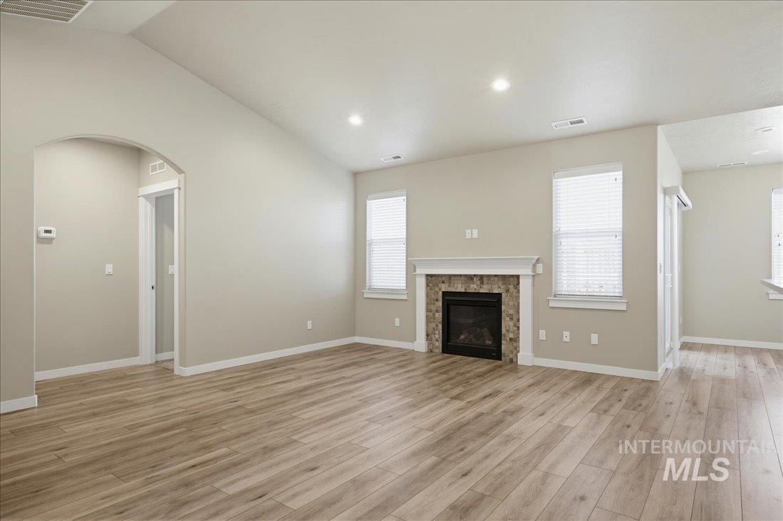 12460 West Azure Street Boise, ID 83713 - Photo 7 of 34 Spacious living area featuring wood-finish flooring, a fireplace with a stone surround and white mantle, vaulted ceilings, recessed lighting, and multiple windows with blinds