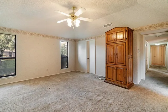 an empty room with chandelier fan and windows