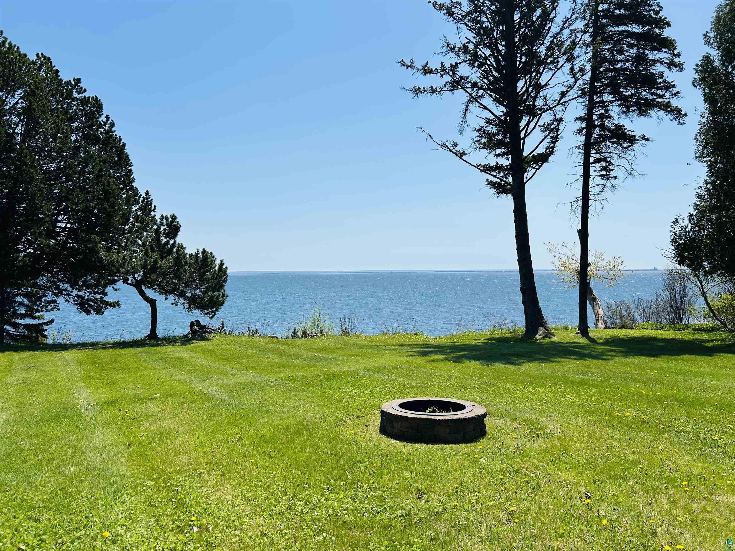 5090 London Road, Unit 1 Duluth, MN 55804 - Photo 42 of 54 Expansive green lawn with a built-in fire pit, mature evergreen trees, and direct waterfront access