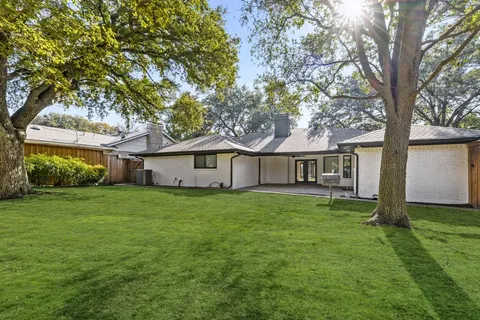 a house that is sitting in the grass with large trees and wooden fence