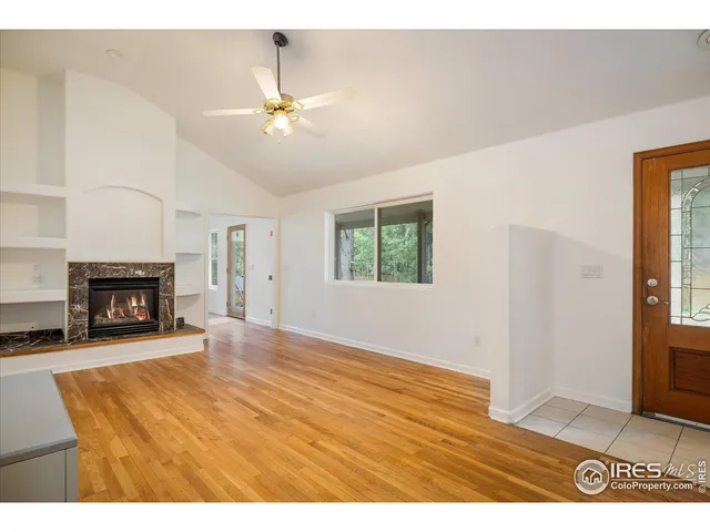 a view of an empty room with wooden floor fireplace and a window