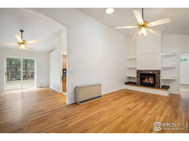 a view of a livingroom with a fireplace a ceiling fan and wooden floor