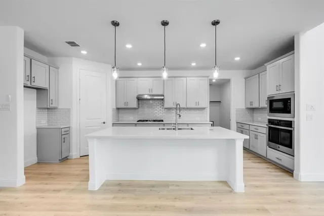 a large kitchen with stainless steel appliances kitchen island a stove a refrigerator a sink dishwasher a oven and a dining table with wooden floor