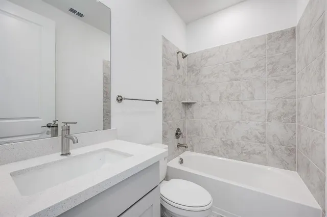 a bathroom with a granite countertop bathtub shower sink vanity and toilet