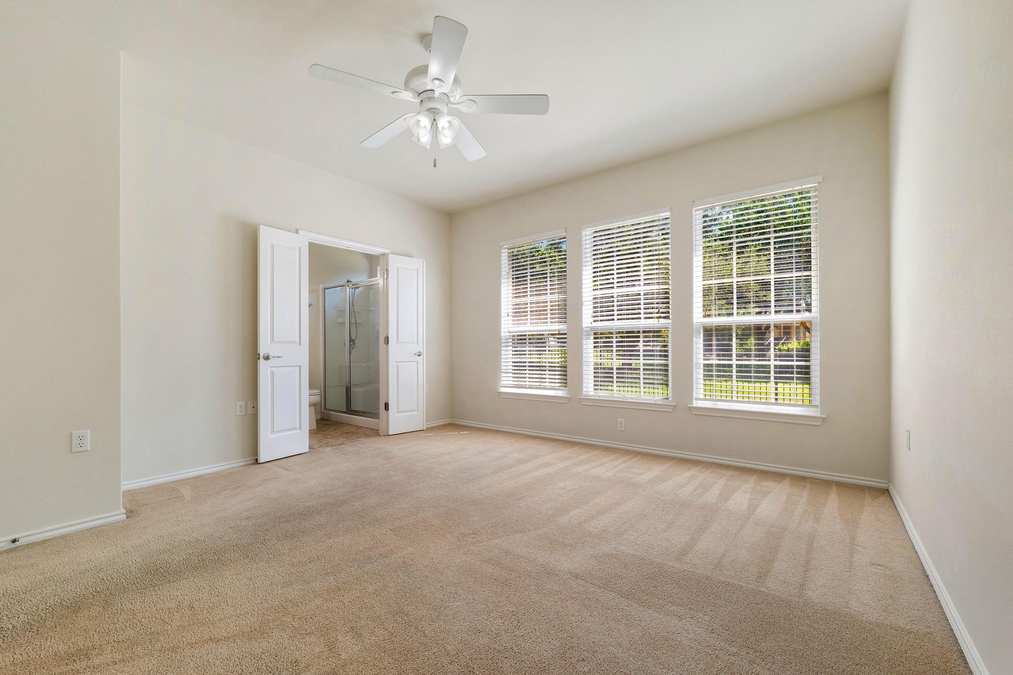 520 Mill Pond Path Georgetown, TX 78633 - Photo 25 of 38 Well-lit primary bedroom features soft carpeting, a ceiling fan, and a convenient ensuite bathroom access.