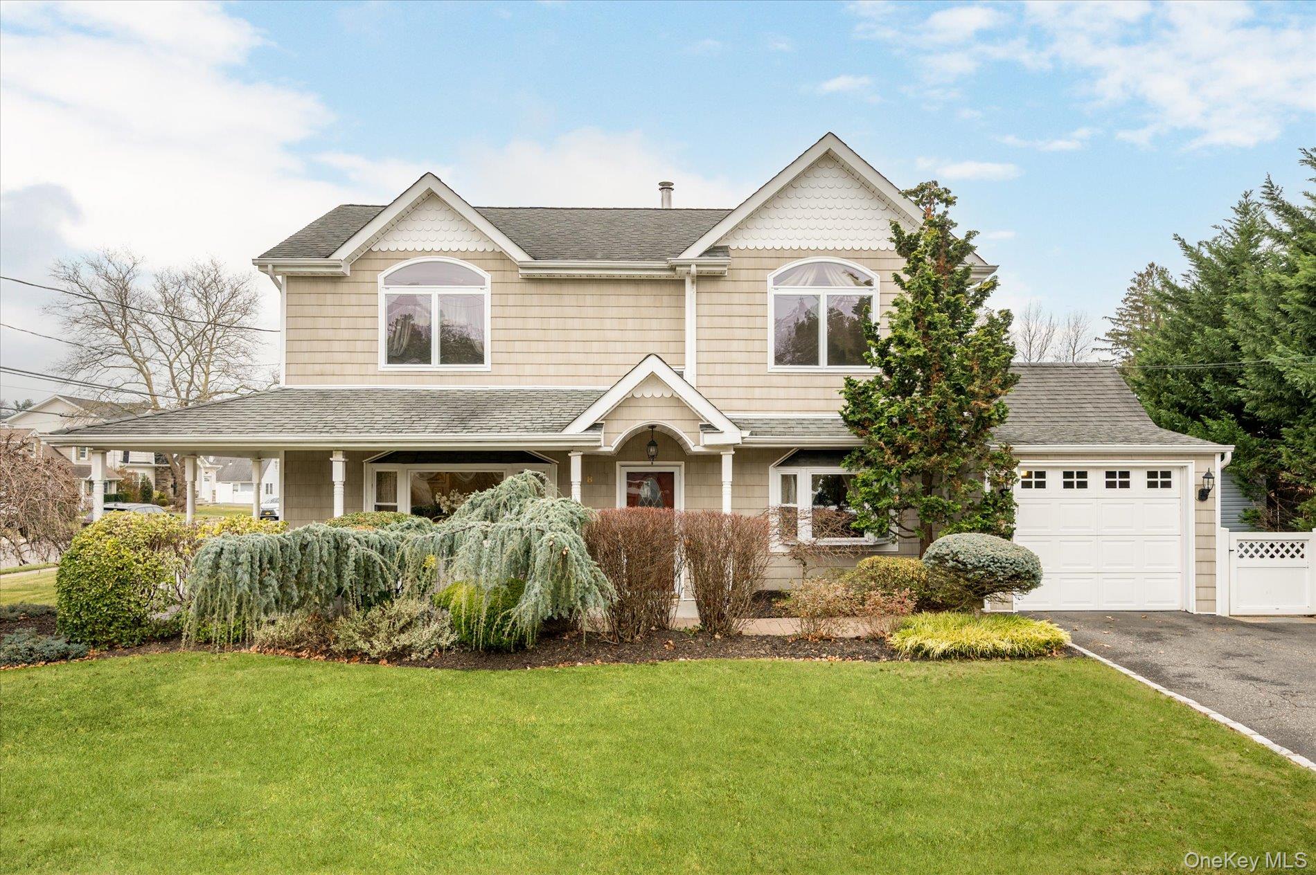 View of front facade featuring a front yard, roof with shingles, driveway, a porch, and an attached garage