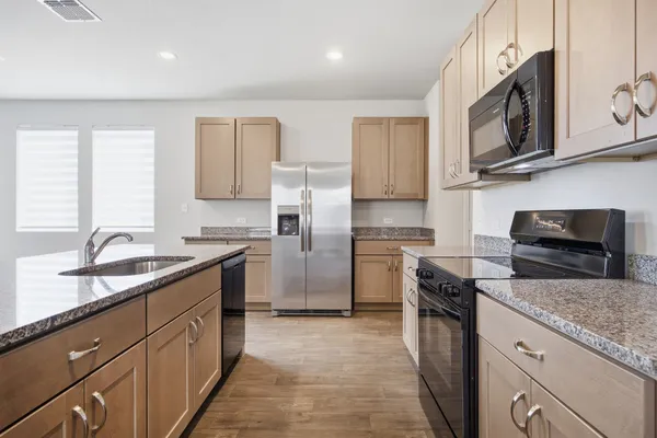 a kitchen with stainless steel appliances granite countertop a stove top oven a sink a refrigerator white cabinets and wooden floor