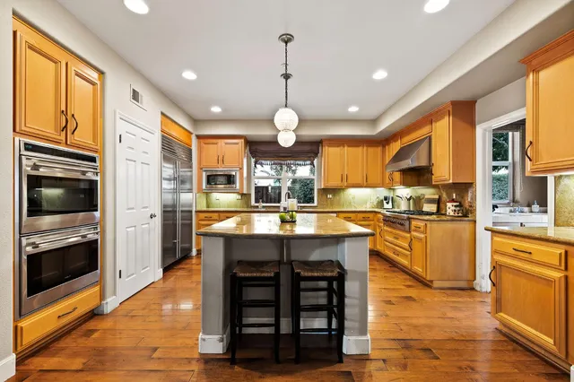 a large kitchen with granite countertop a stove top oven a sink dishwasher a dining table and chairs with wooden floor