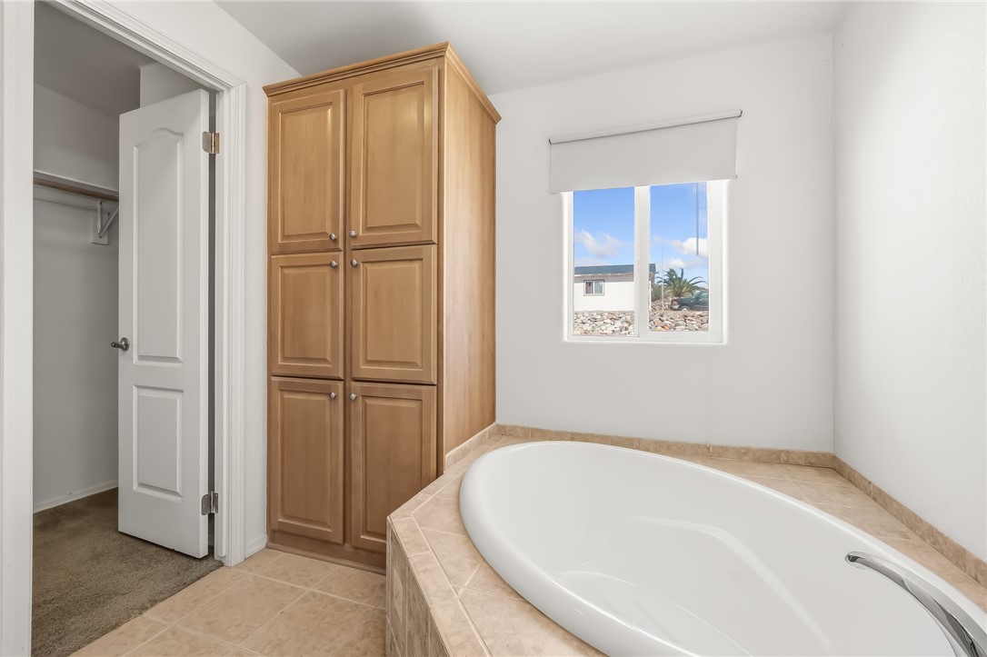2525 South Ridge Avenue Bullhead City, AZ 86429 - Photo 43 of 76 Soaking tub with tiled surround, built-in storage cabinetry, a window with roller shade, and tiled flooring