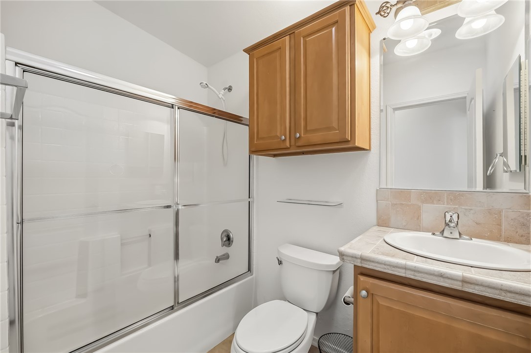 2525 South Ridge Avenue Bullhead City, AZ 86429 - Photo 56 of 76 Guest Bathroom featuring a full tub with sliding glass doors, a vanity with an integrated sink and tile countertop, wood-finish cabinetry, and an overhead lighting fixture