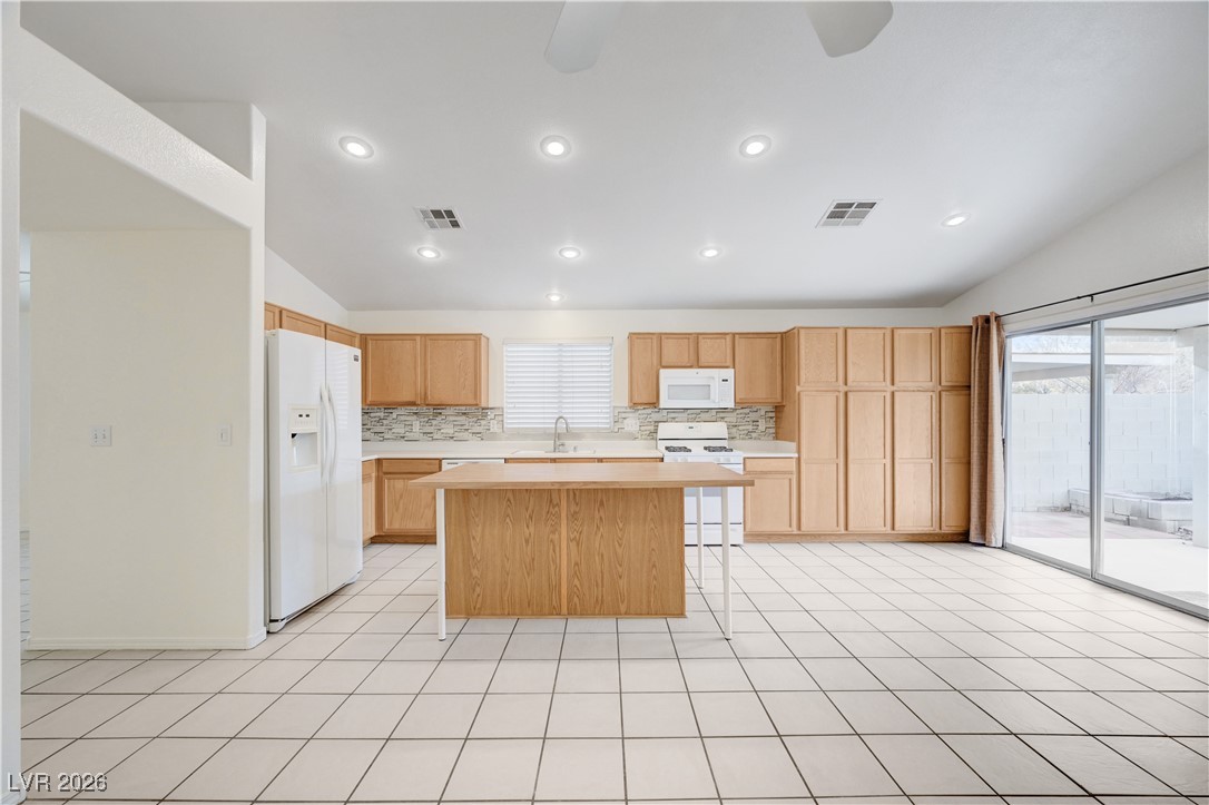 9929 Princess Cut Street Las Vegas, NV 89183 - Photo 16 of 52 Kitchen featuring vaulted ceiling, light countertops, white appliances, a center island, and backsplash