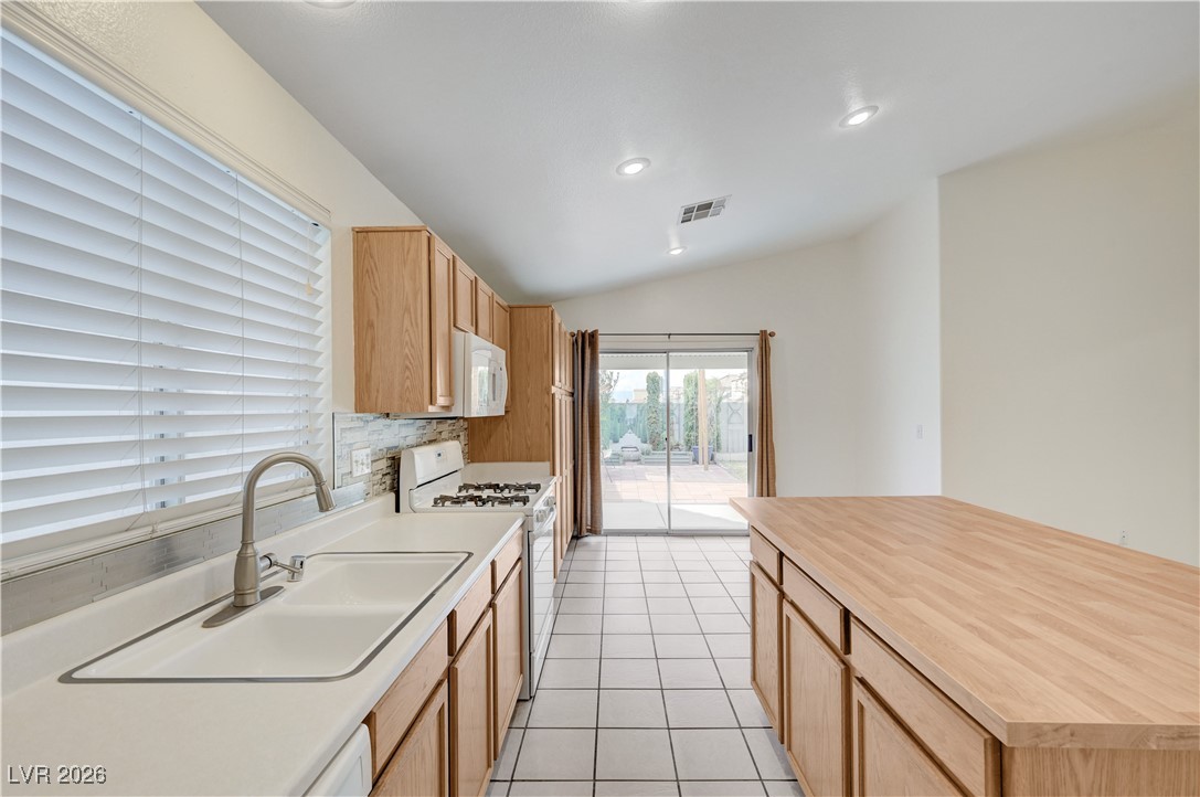9929 Princess Cut Street Las Vegas, NV 89183 - Photo 23 of 52 Kitchen featuring white appliances, light countertops, light brown cabinets, light tile patterned floors, and decorative backsplash