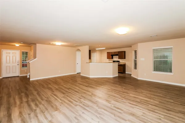 a view of empty room with wooden floor and kitchen