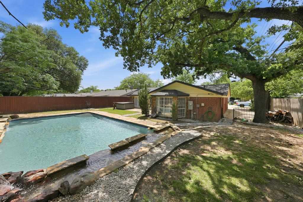 1108 Billie Ruth Lane Hurst, TX 76053 - Photo 25 of 27 Expansive backyard featuring a rectangular in-ground pool with stone coping, a decorative stone water feature, a red brick and siding exterior, mature trees, and a privacy fence