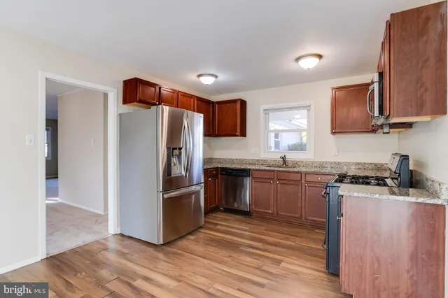 a kitchen with stainless steel appliances granite countertop a stove top oven a sink dishwasher a microwave oven and a refrigerator with wooden floor