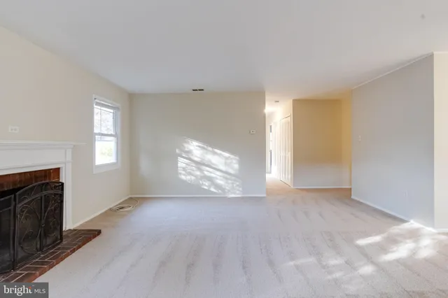 a view of an empty room with wooden floor fireplace and a window