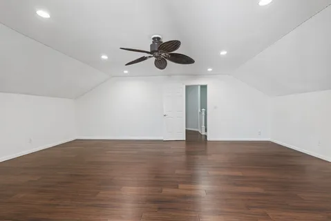a view of an empty room with wooden floor and a ceiling fan
