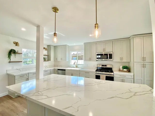 a large kitchen with stainless steel appliances kitchen island granite countertop a refrigerator a sink a stove and white cabinets with wooden floor