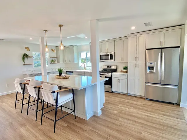 a kitchen with stainless steel appliances a refrigerator a stove a sink dishwasher and a dining table with wooden floor