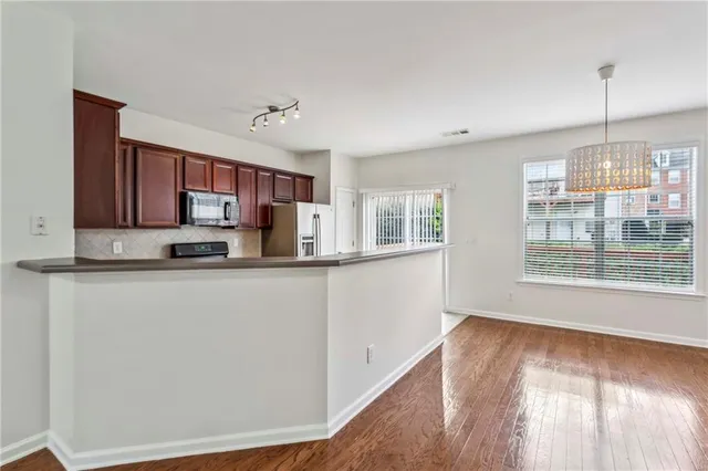 a kitchen with stainless steel appliances granite countertop a stove a sink dishwasher a refrigerator and a dining table with wooden floor