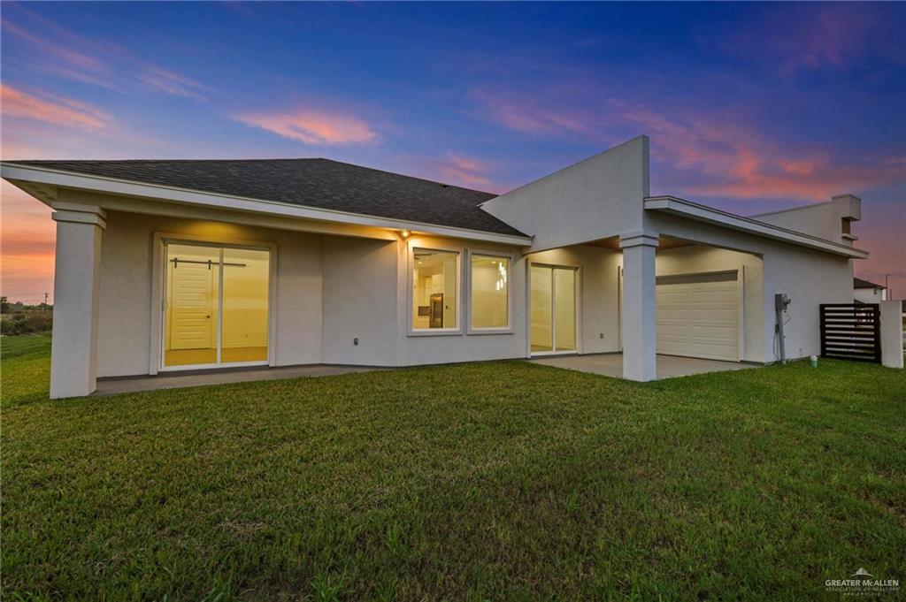 2716 East Conroe Road Edinburg, TX 78542 - Photo 27 of 31 Back of house at dusk with stucco siding, a patio area, a yard, and a shingled roof