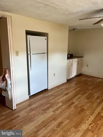 an empty room with wooden floor and a refrigerator