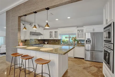 a kitchen with stainless steel appliances granite countertop a sink a stove a refrigerator and island with wooden floor