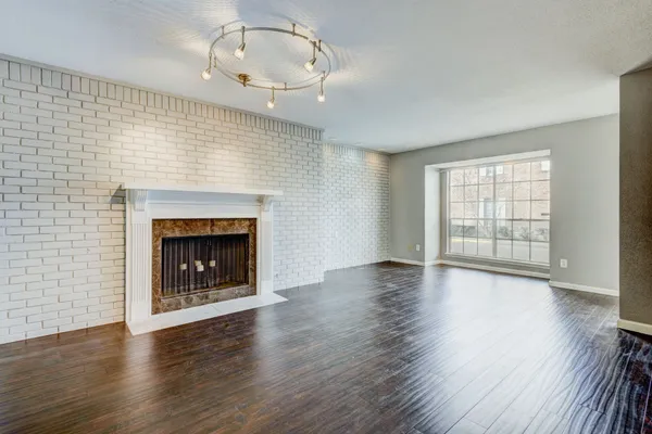 a view of an empty room with wooden floor fireplace and a window