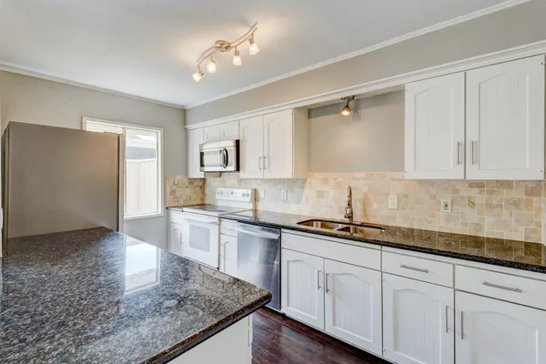 a kitchen with a sink dishwasher a stove and white cabinets with wooden floor