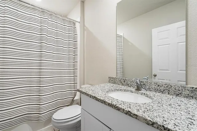 a bathroom with a granite countertop sink toilet a mirror and shower curtain
