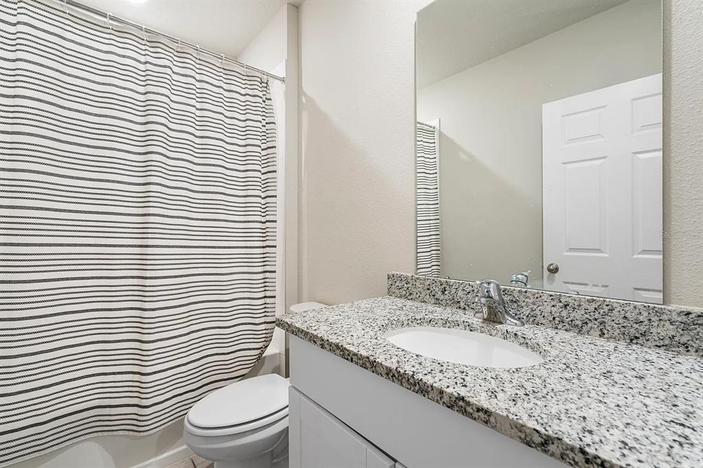 1274 Citrus Landings Boulevard Davenport, FL 33837 - Photo 18 of 20 a bathroom with a granite countertop sink toilet a mirror and shower curtain