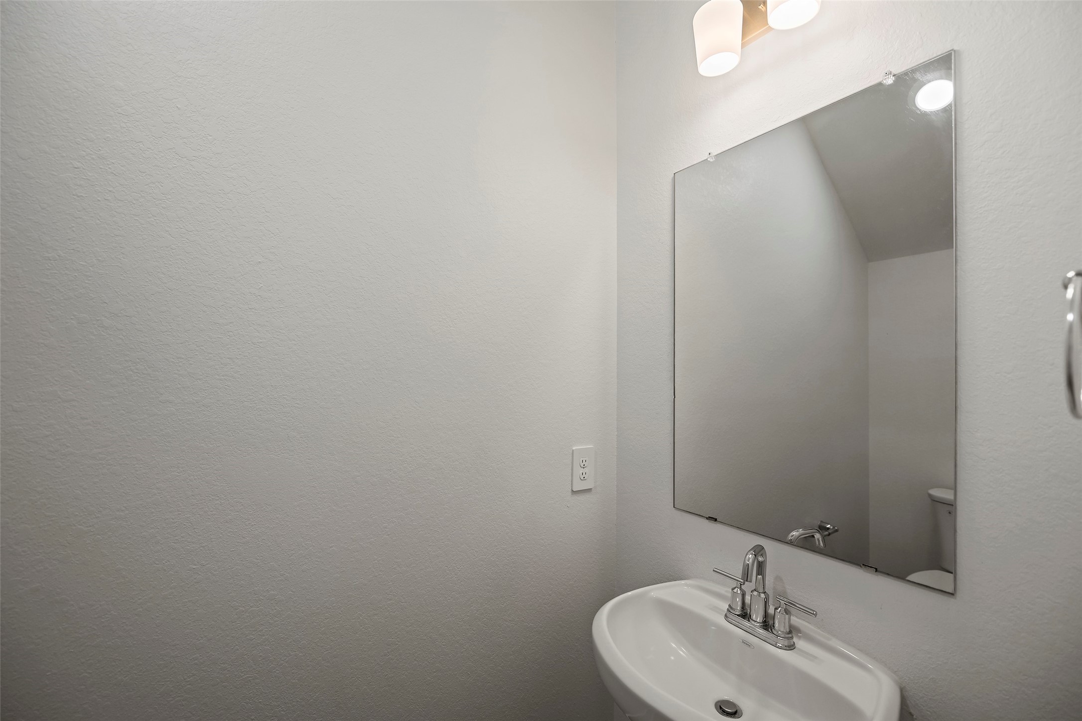10603 Whitejacket Conroe, TX 77385 - Photo 5 of 42 This photo shows a compact, modern half-bathroom with a white pedestal sink, a sleek rectangular mirror, and simple wall-mounted lighting.
