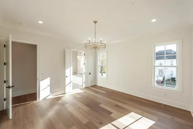 an empty room with wooden floor chandelier fan and windows