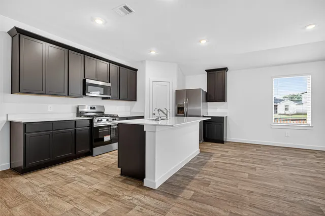 a kitchen with stainless steel appliances kitchen island granite countertop a stove top oven a sink dishwasher and a refrigerator with wooden floor