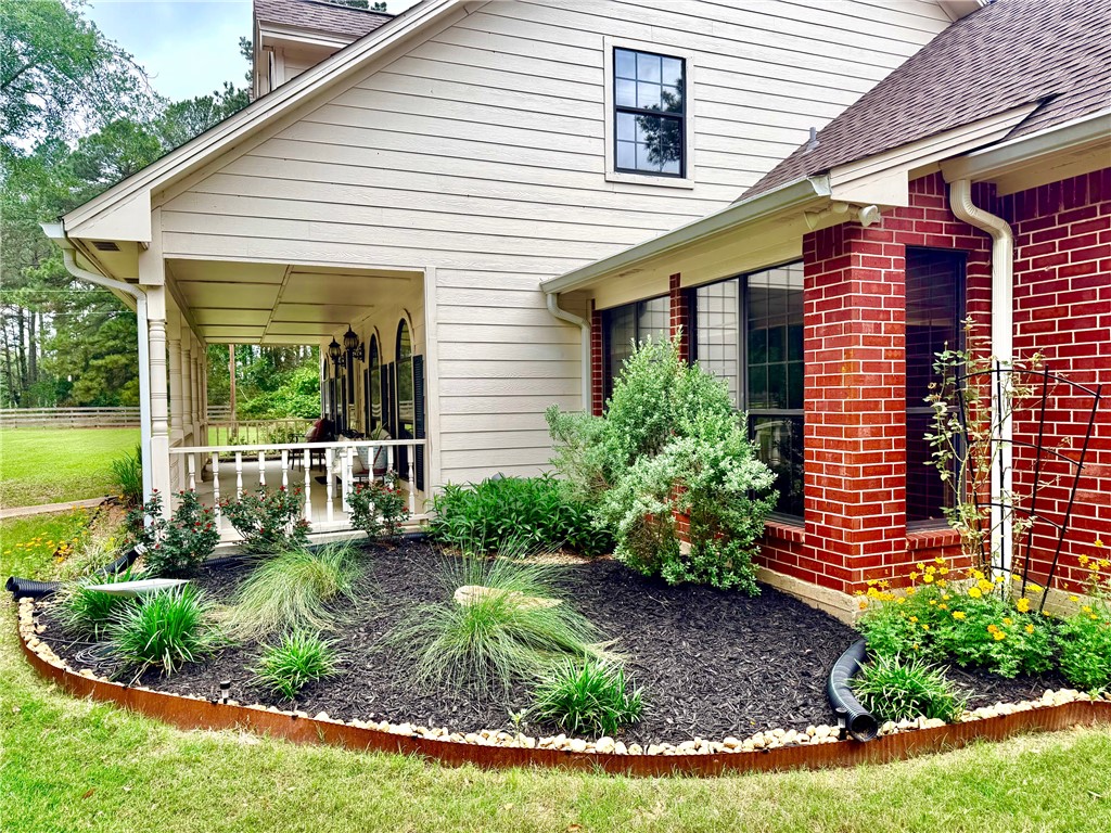 31928 Reids Prairie Road Waller, TX 77484 - Photo 4 of 43 Exterior featuring brick and horizontal siding, a covered porch with white railings, and a well-maintained landscaping bed with dark mulch and various plantings