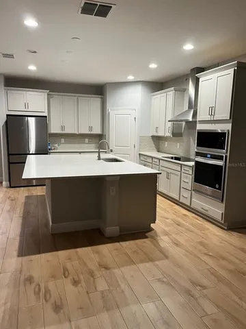 a large kitchen with stainless steel appliances kitchen island granite countertop a stove a refrigerator a sink dishwasher and white cabinets next to a window