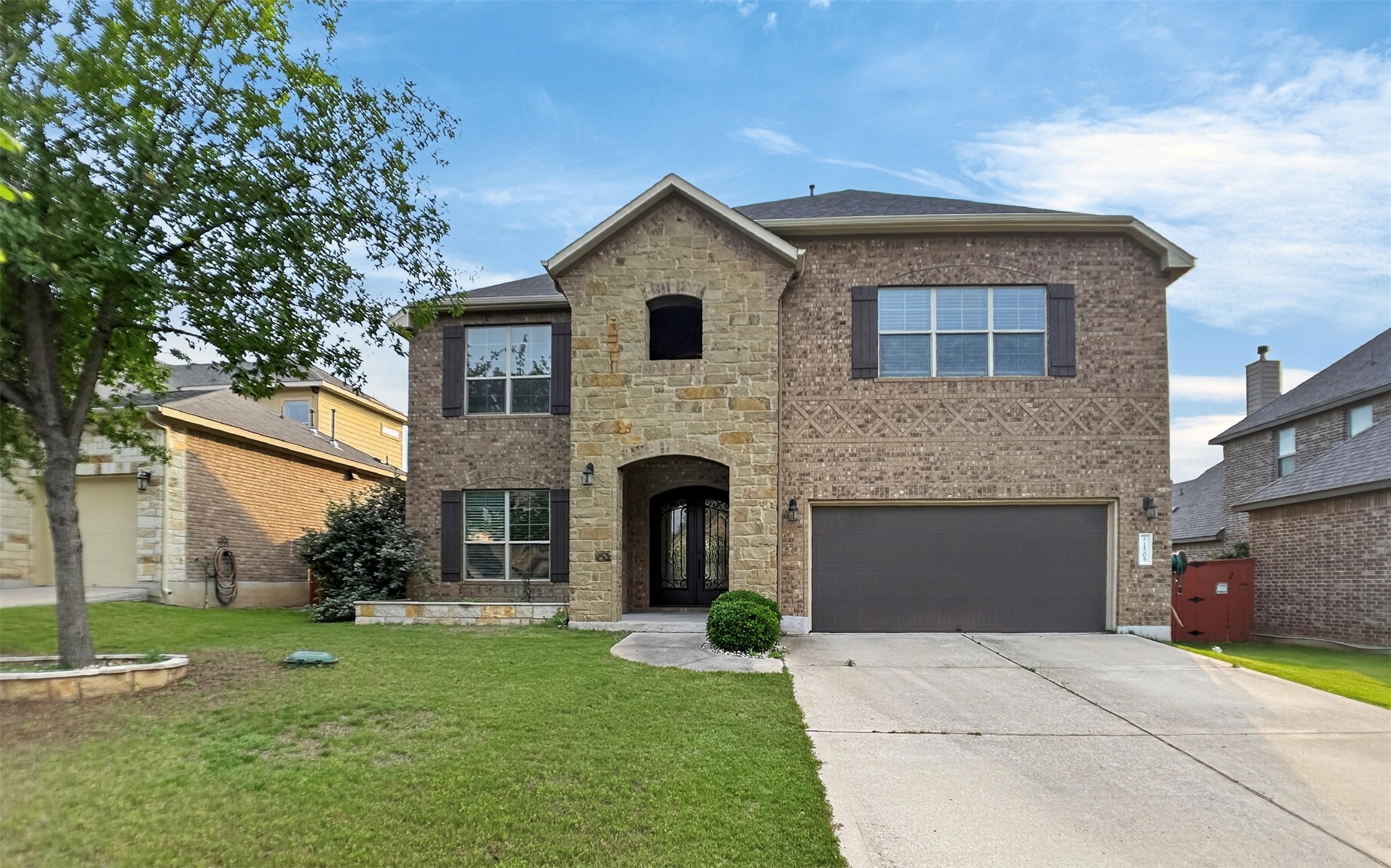 Two-story residence featuring a brick and stone facade, arched entry, dark wood shutters, and an attached two-car garage