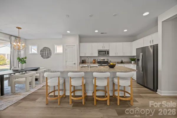 a kitchen with stainless steel appliances granite countertop a refrigerator a stove a sink a dining table and chairs with wooden floor
