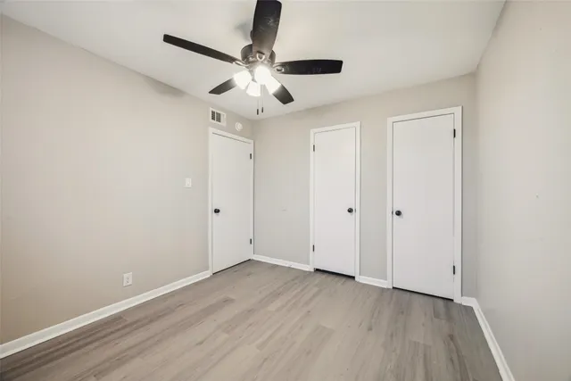 an empty room with wooden floor fan and windows