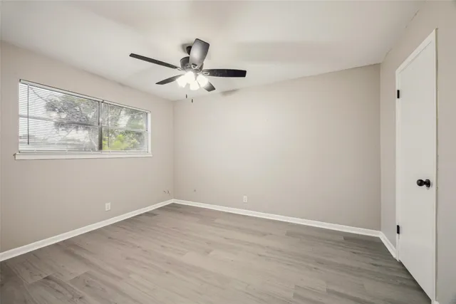 a view of an empty room with wooden floor and a ceiling fan