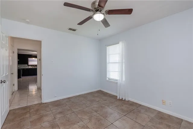 an empty room with chandelier fan and windows