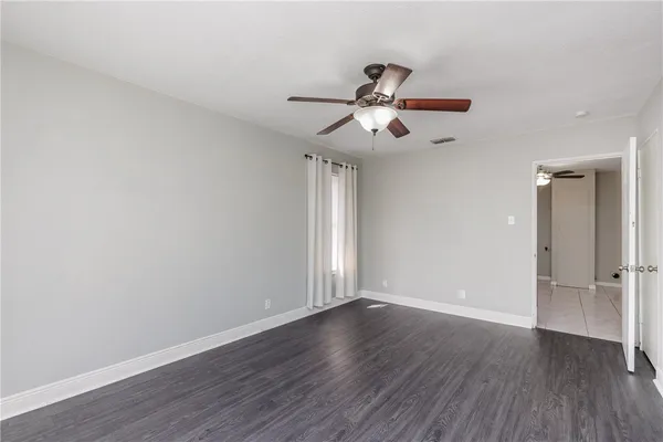 an empty room with wooden floor fan and windows
