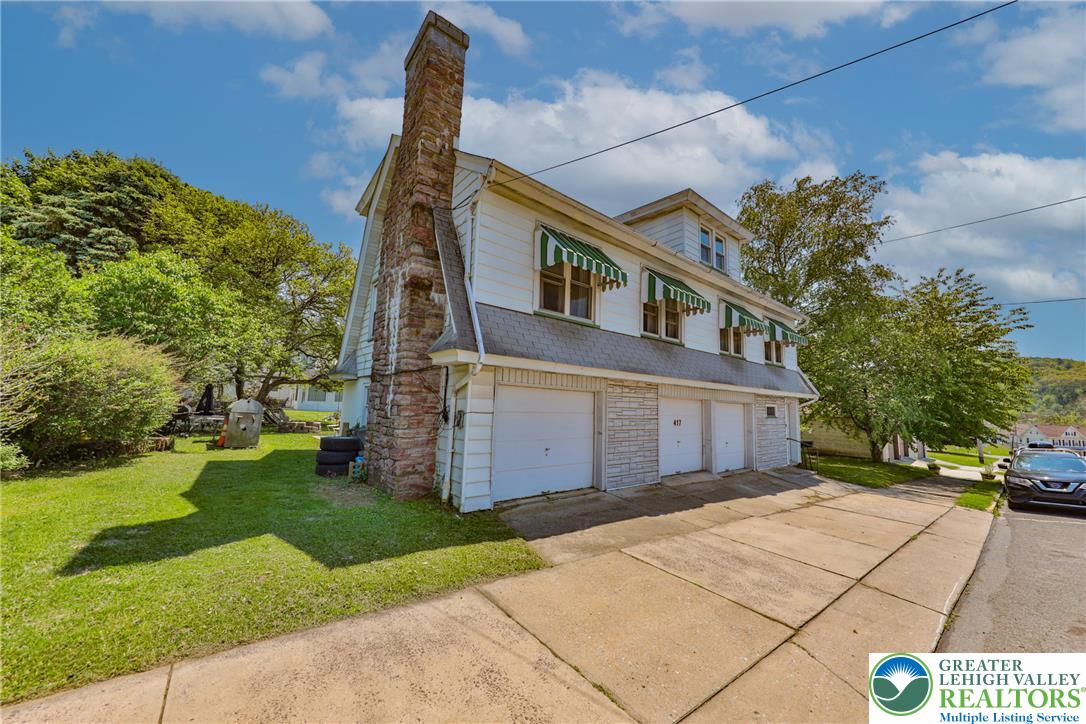 417 3rd Street Lehighton, PA 18235 - Photo 35 of 39 This multi-level residence features a stone chimney and three garage doors, all set against a vibrant green lawn.
