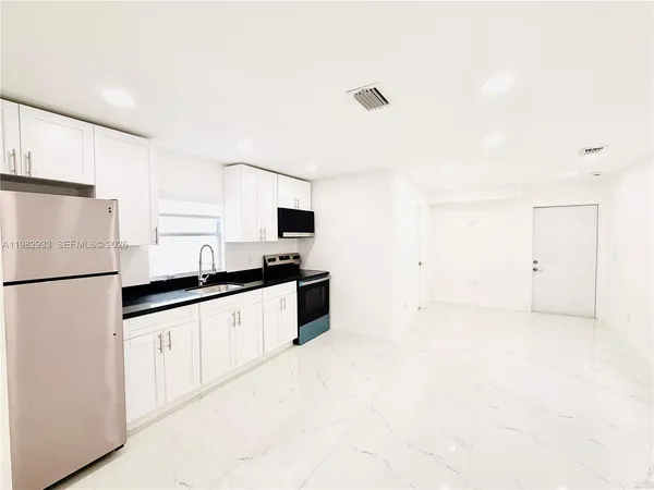a kitchen with granite countertop a refrigerator a stove a sink and white cabinets