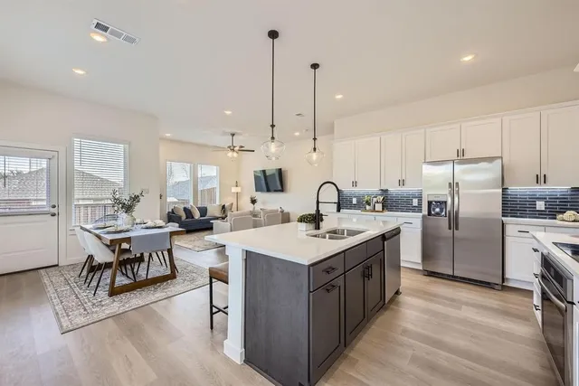 a open kitchen with stainless steel appliances granite countertop a stove a sink dishwasher a refrigerator and a dining table with wooden floor