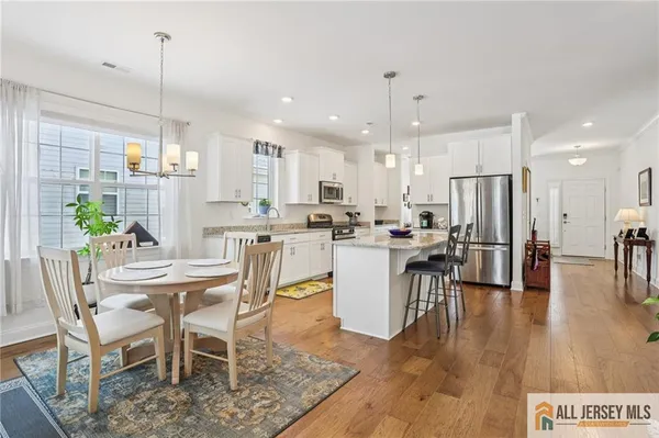 a dining room kitchen with stainless steel appliances kitchen island granite countertop a dining table chairs and white cabinets